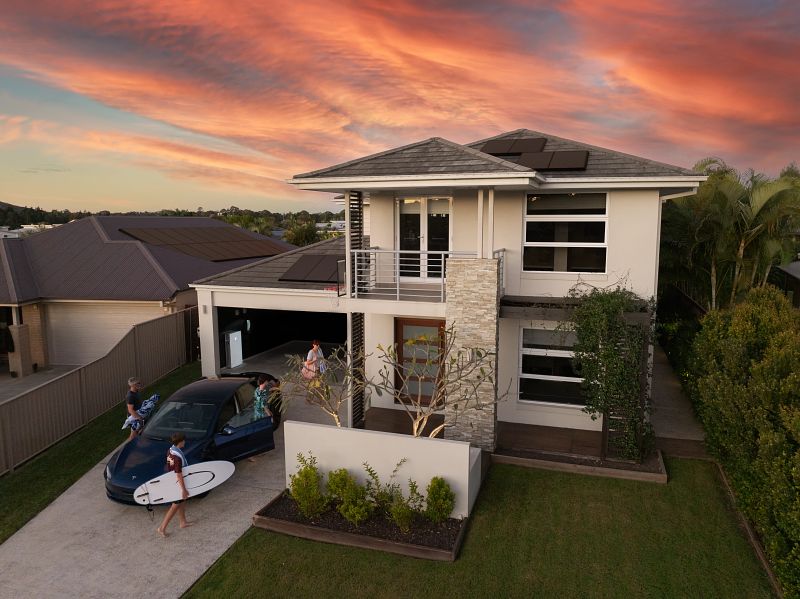 Tesla Powerwall 3 installed in two-storey new home with a dark blue Tesla Model 3 and family in the driveway